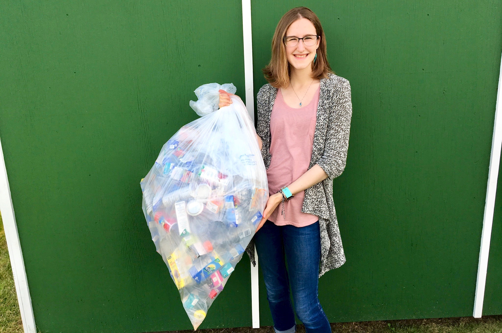 Veronika adolescente tient un sac poubelle blanc rempli de bouteilles recyclées. 