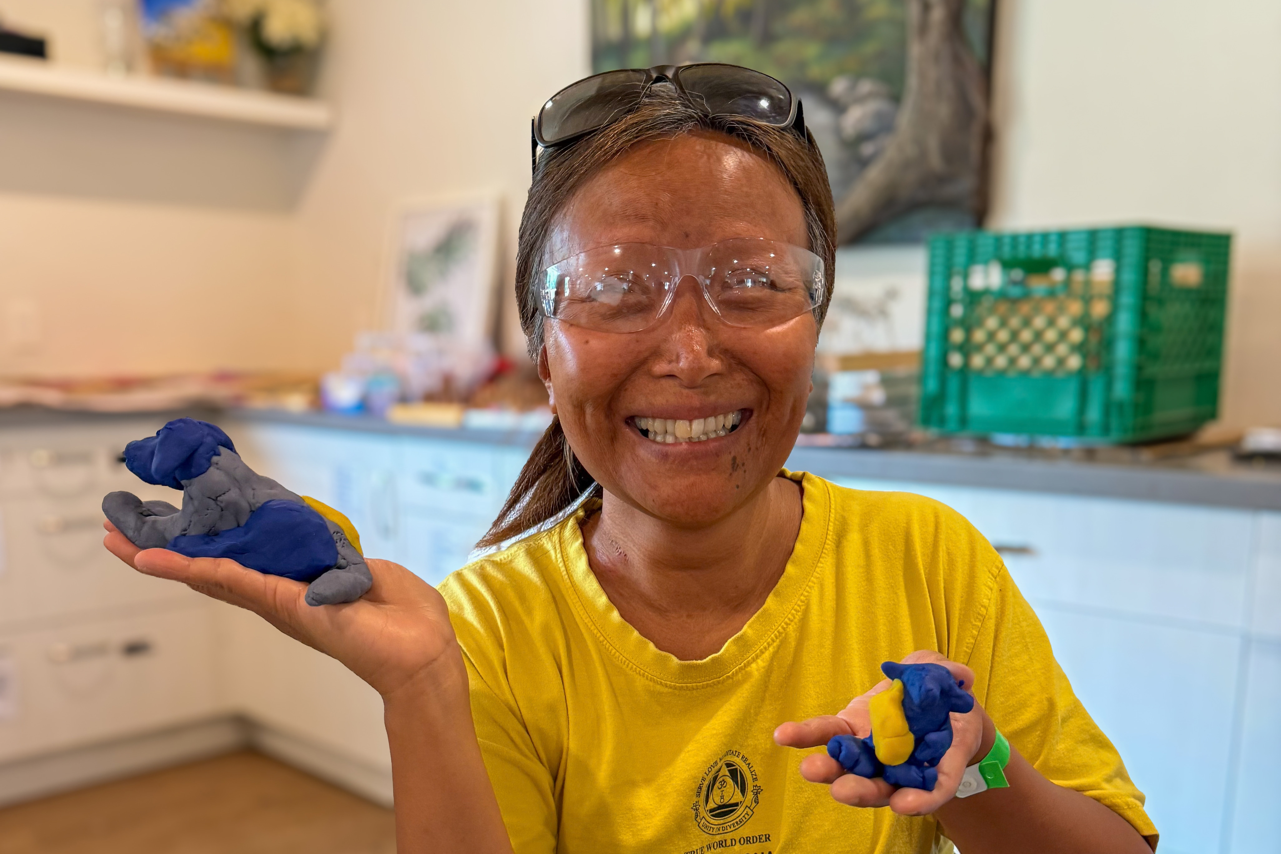 Vivian, a CNIB Lake Joe Young Adults Arts Intensive Week participant, smiles while holding up two small clay statues she made.