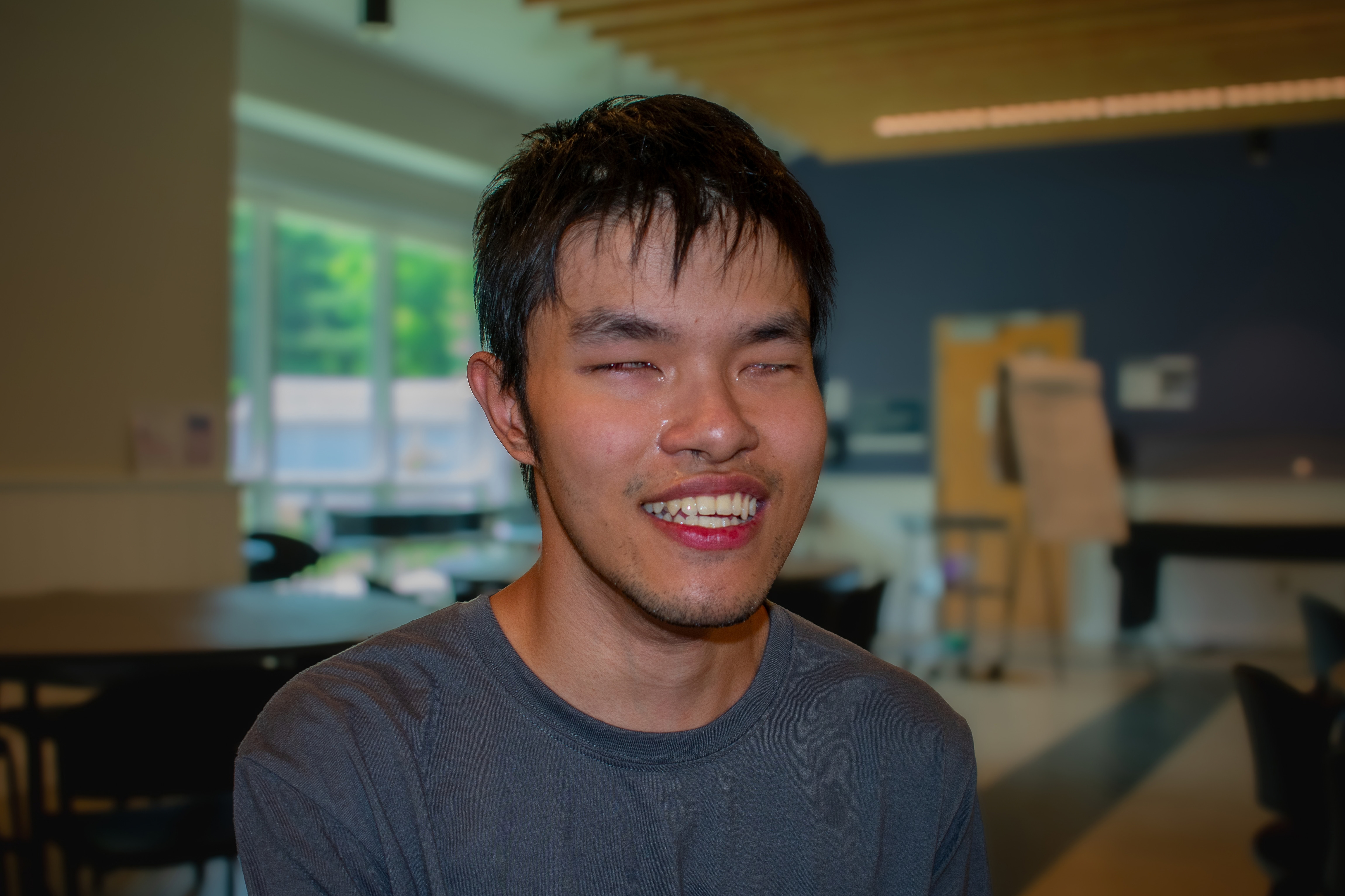 William, a CNIB Lake Joe Young Adults Arts Intensive Week participant, smiles while sitting in a dining hall.