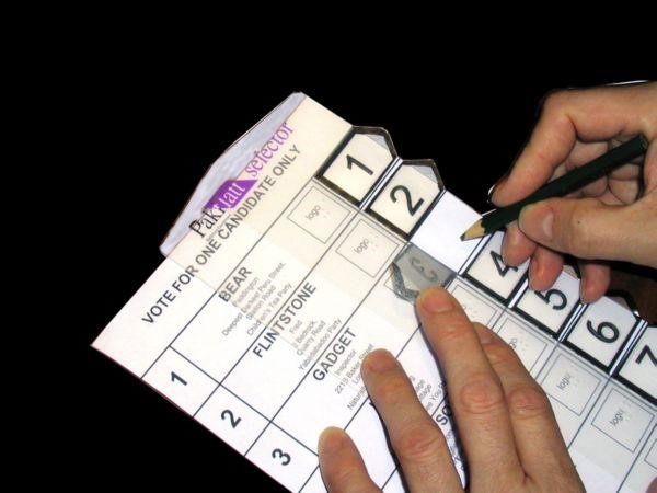 A hand using a pencil is marking a ballot using a braille template
