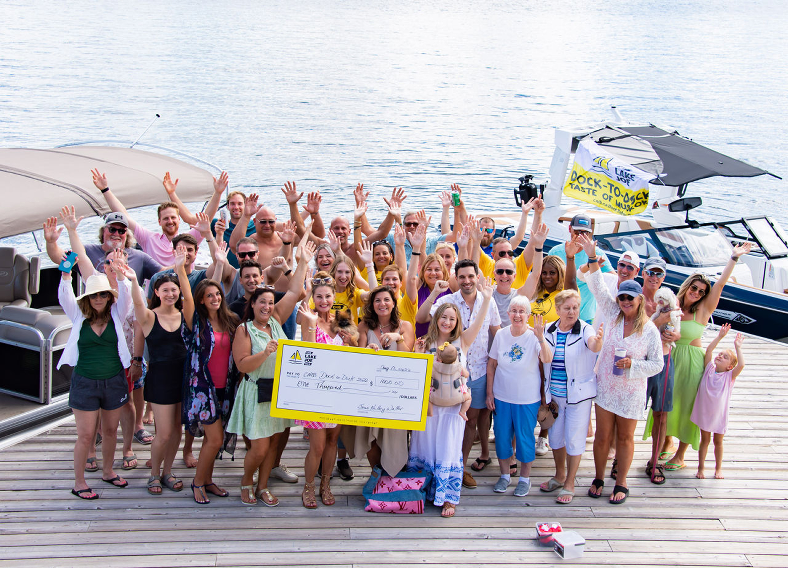 A group of people smiling and waving holding up a large cheque made out to CNIB on a dock