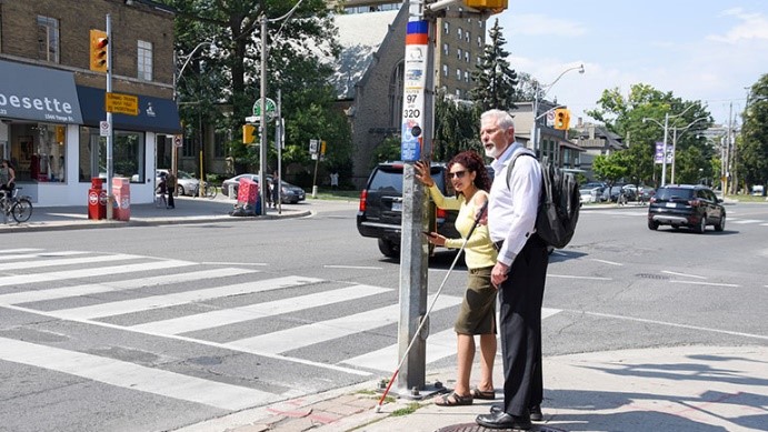 Photo of man with white cane standing at an intersection.