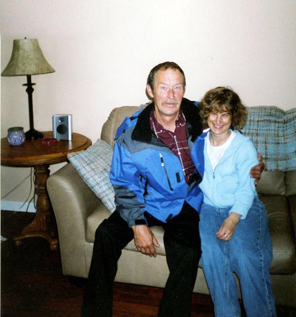 Holly Bartlett smiling, arm-in-arm with her father in a living room