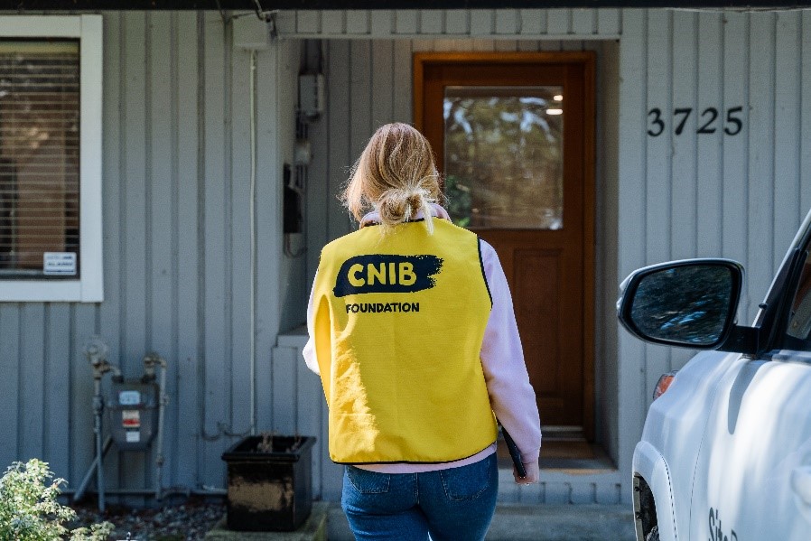 A CNIB Fundraiser in a branded yellow vest approaching a front door