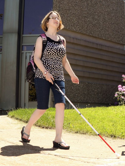 A woman who is blind walks down the street, she is using a White Cane