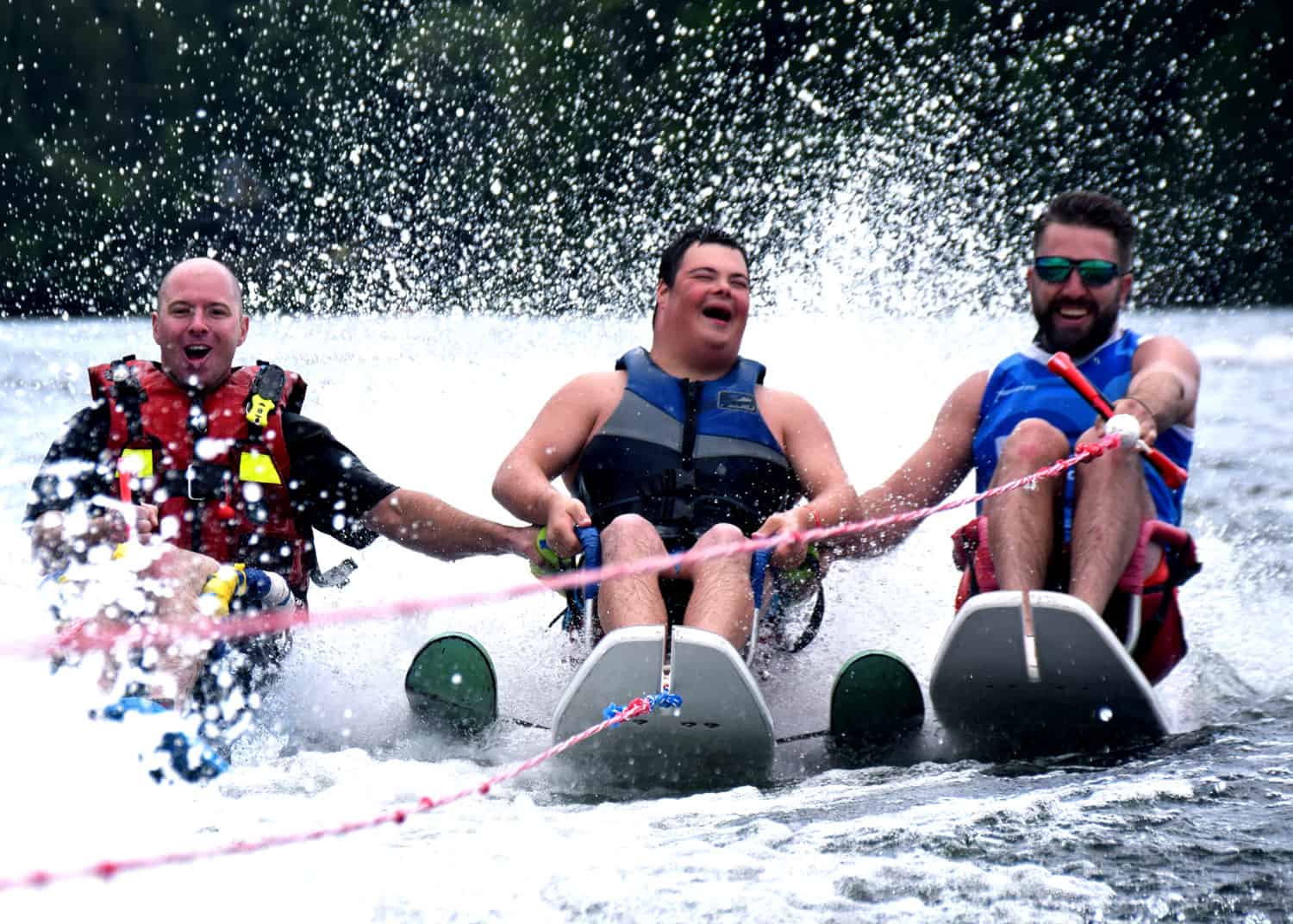 trois hommes font du ski nautique. Celui du centre est en fauteuil roulant.