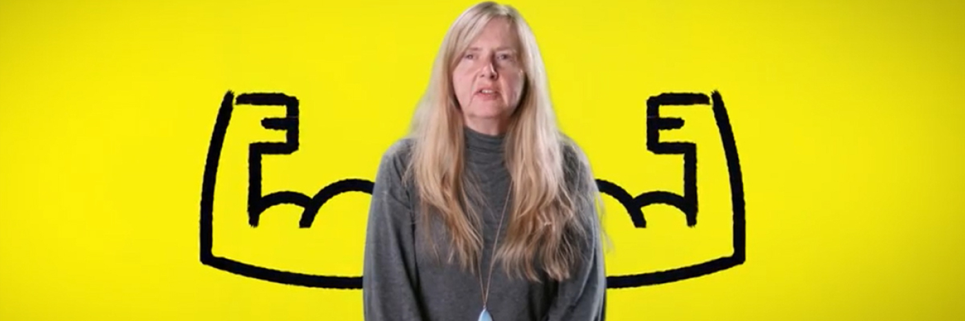 A woman in front of a yellow background with a cartoon drawing of flexed arms on either side of her. 