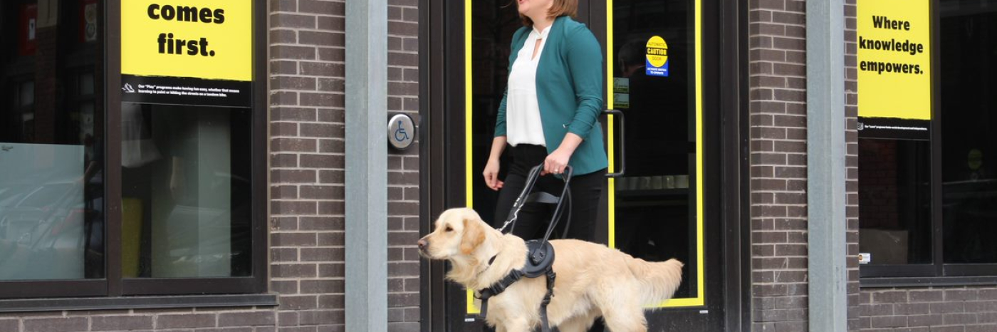 Erin Malone and her golden retriever guide dog, Winston, walking in front of a CNIB.