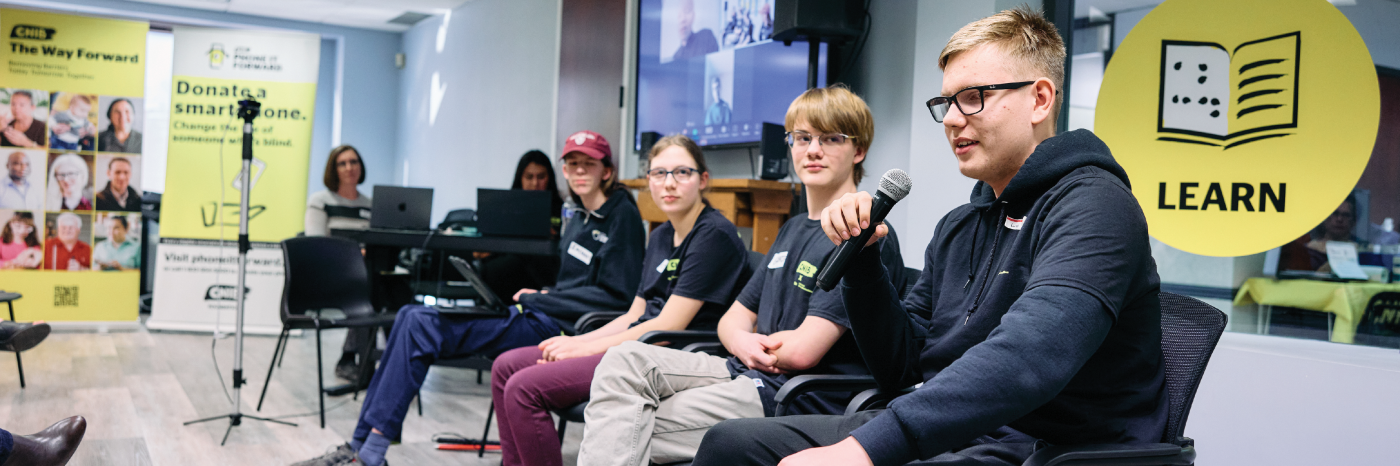 A panel of four youths sit in a line at the front of the room in the CNIB Calgary office