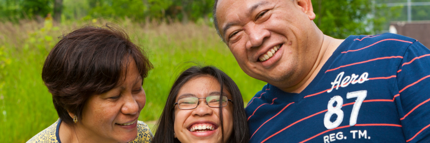 A mother, father, and teenage daughter laugh together; the daughter is wearing glasses.