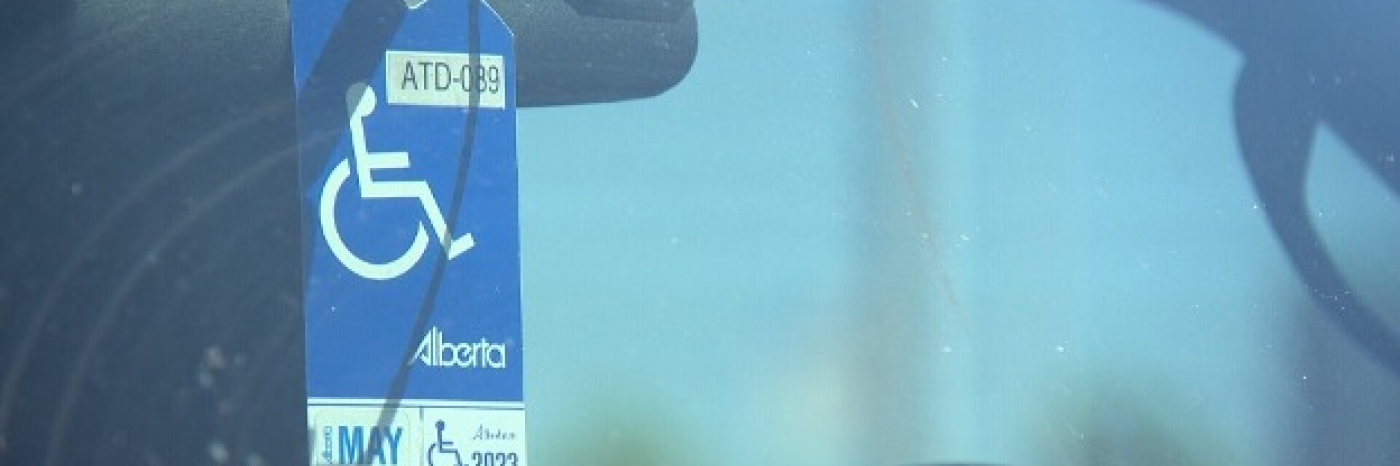 An Alberta accessible parking permit is hung on a car's rear-view mirror. The photo is taken from outside the vehicle, looking through the windshield.