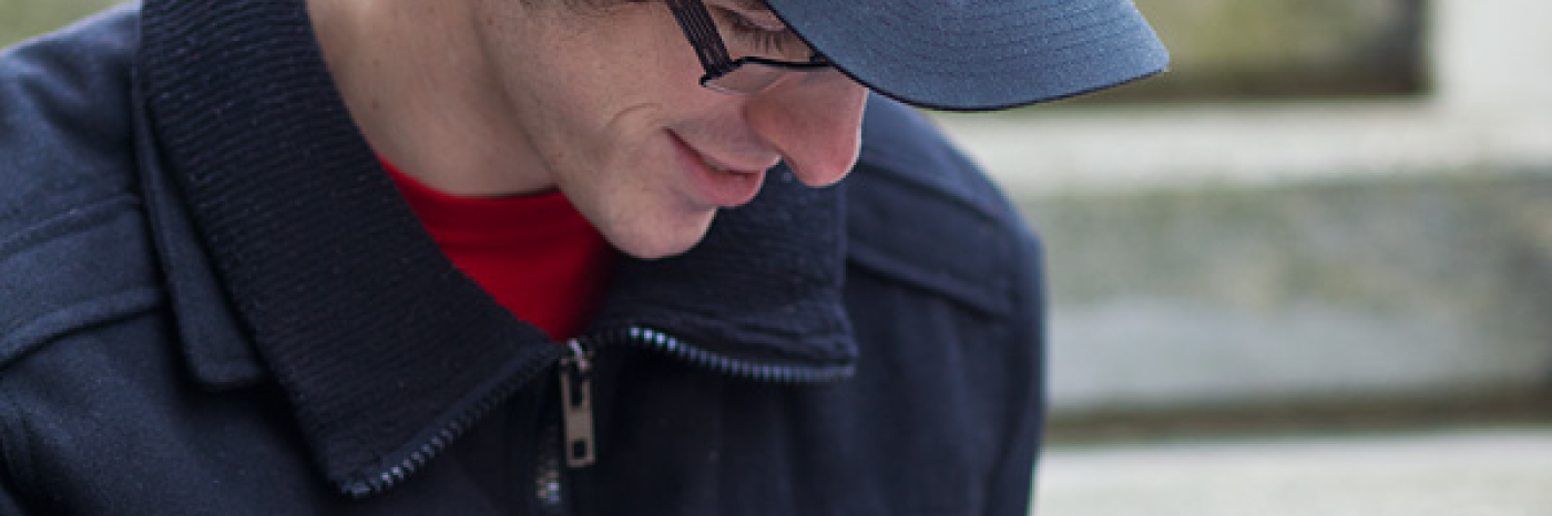 Man in black baseball cap looking through red magnifier