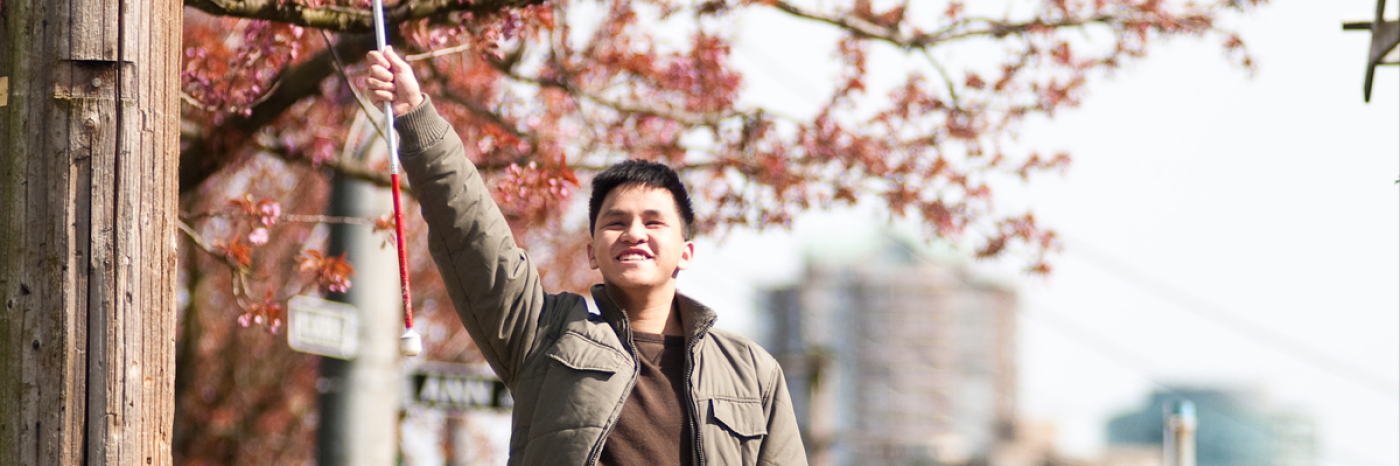 Male teenager triumphantly raising his white cane into the air.