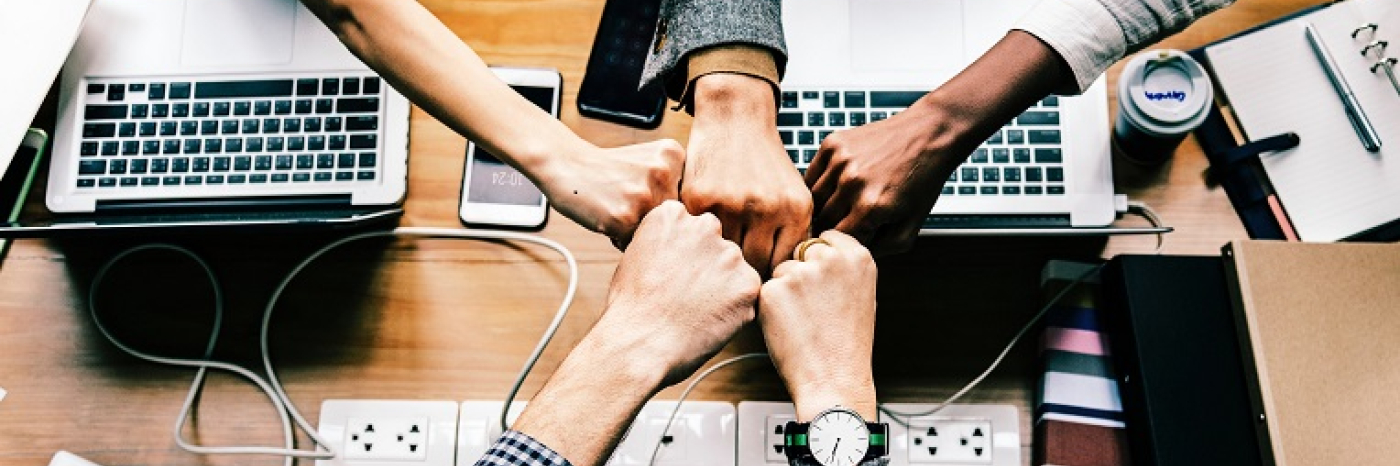 A diverse group of people in a circle fist bump on another in collaboration