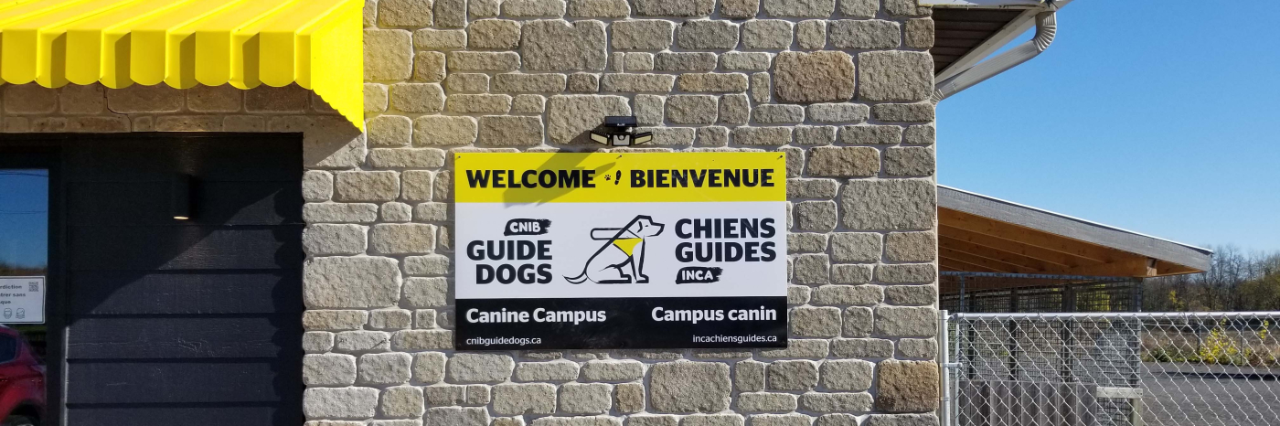 A photo of the welcome sign placed on the exterior of the Canine Campus. It reads: “Welcome & Bienvenue” with the CNIB Guide Dogs logo in the middle of the sign.