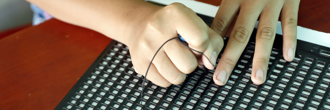 A young child's hands write with a slate and stylus.