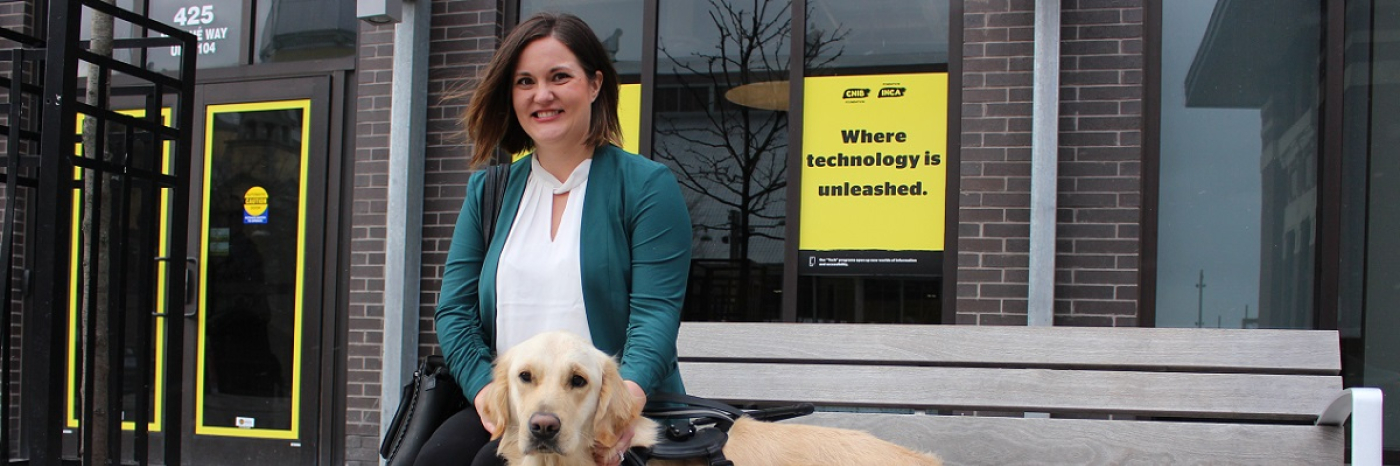 A smiling woman sitting on a bench with her CNIB Guide Dog, outside a CNIB building with yellow branded CNIB signs and posters. 