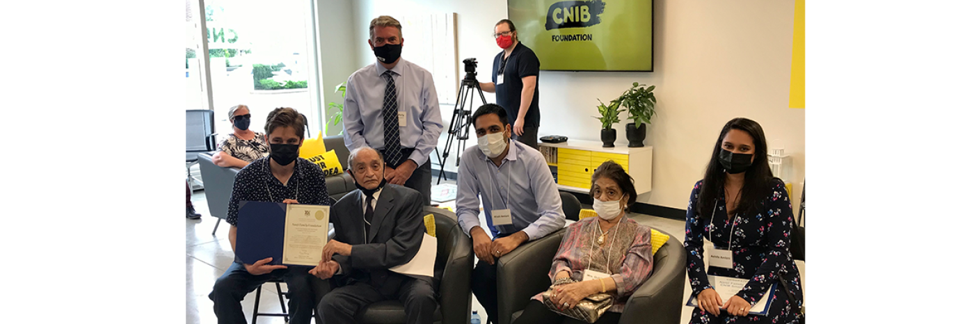 John Rafferty, President and CEO of CNIB stands behind by four members of the Nanji Family. On the left, Hale Mahon presents a certificate to the Nanji family on behalf of the MPP’s office in Barrie. The group poses for a photo inside the newly renovated Nanji Family Foundation CNIB SmartLife Centre in Barrie, Ontario.