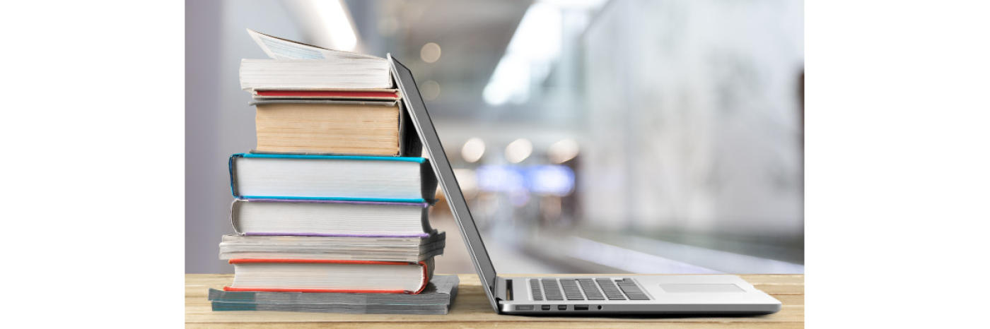 A stack of books beside a laptop on a wooden table. 