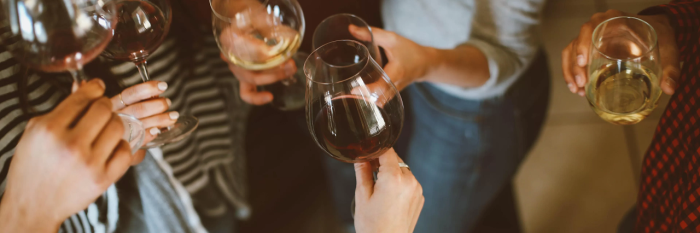A group of people drinking wine. They are hosting in their drinks in the air and raising a toast.