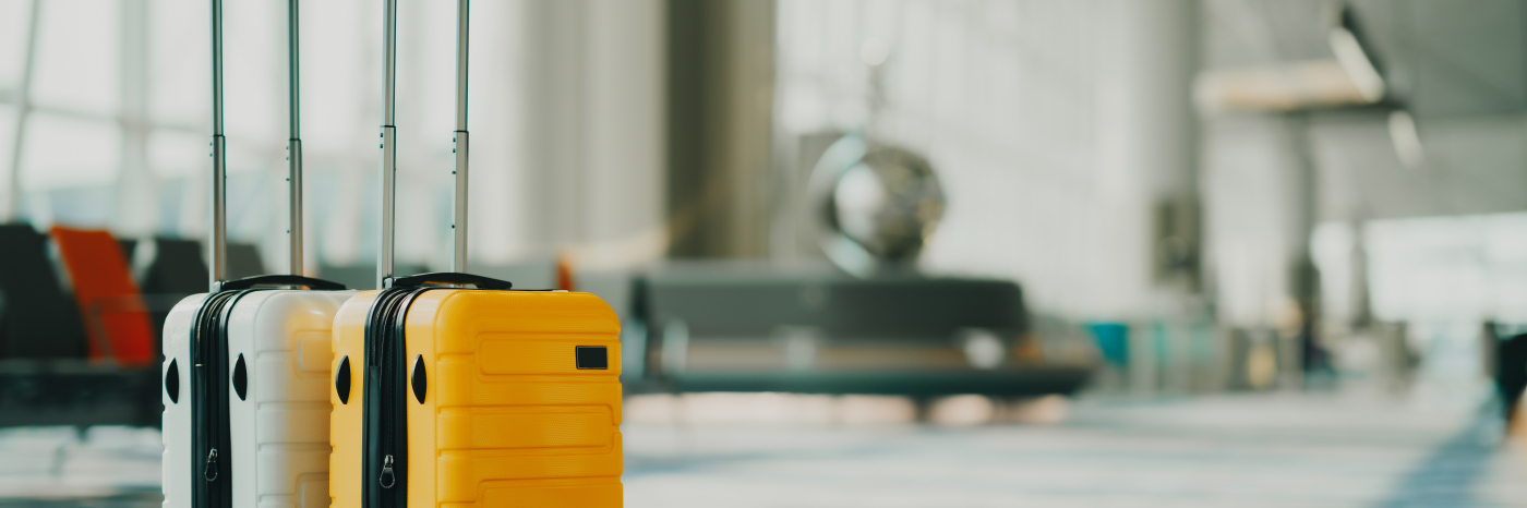 Two suitcases sit in an airport terminal near a departure gate.