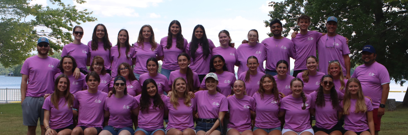 The 2026 seasonal staff team is posing on the lawn. There are 34 people wearing shorts and pink tshirts.
