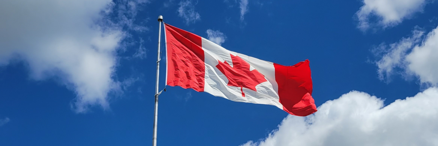 A Canadian flag waves on a flagpole against a bright blue cloudy sky.