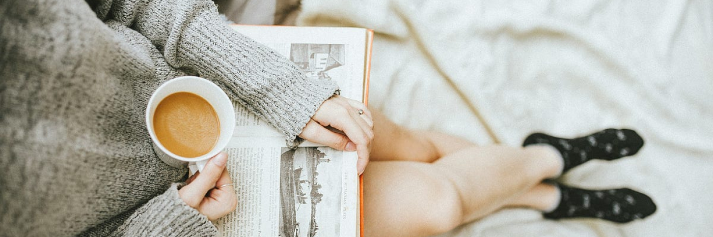 Birds eye view photo of a woman sitting with a coffee and a book on her lap.