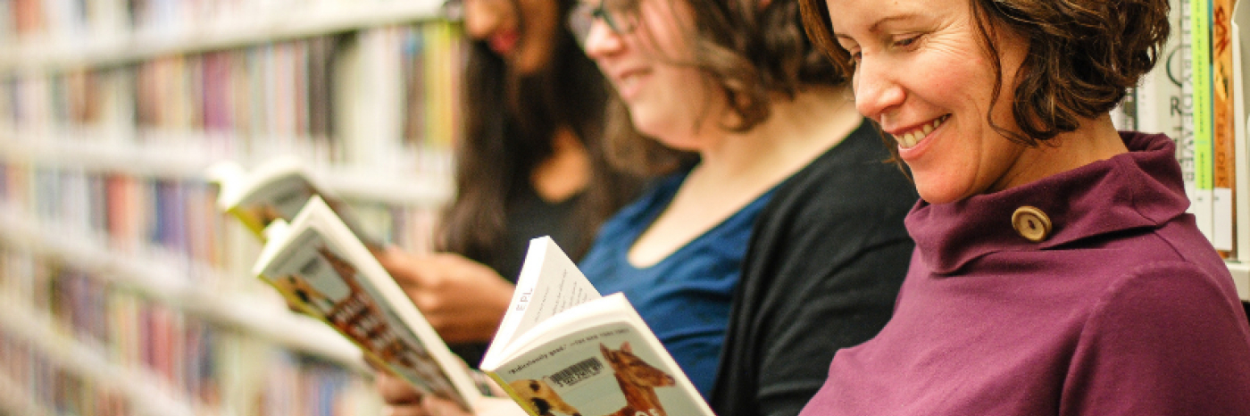 Three women standing in front of a row of bookshelves each reading a book.