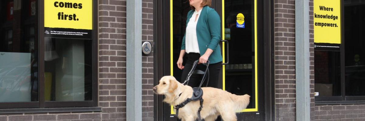 Erin Malone et son chien-guide, un golden retriever, passant devant un bureau d’INCA.