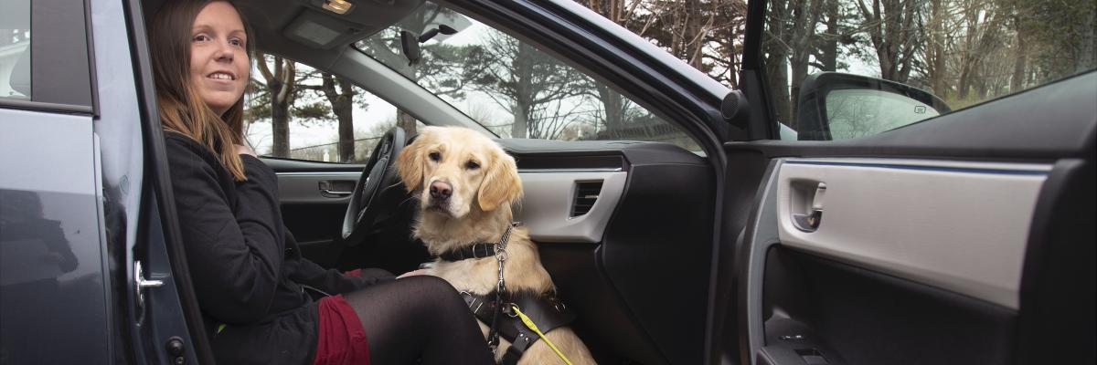 Kelly and her guide dog Maple, sitting in the passenger side of a car with the door open – smiling for the camera.