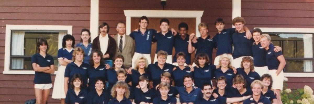 Photo of the 1986 staff team (35 men and women in blue golf shirts and white shorts) posing outside the staff building for CNIB Lake Joe’s 25th anniversary.