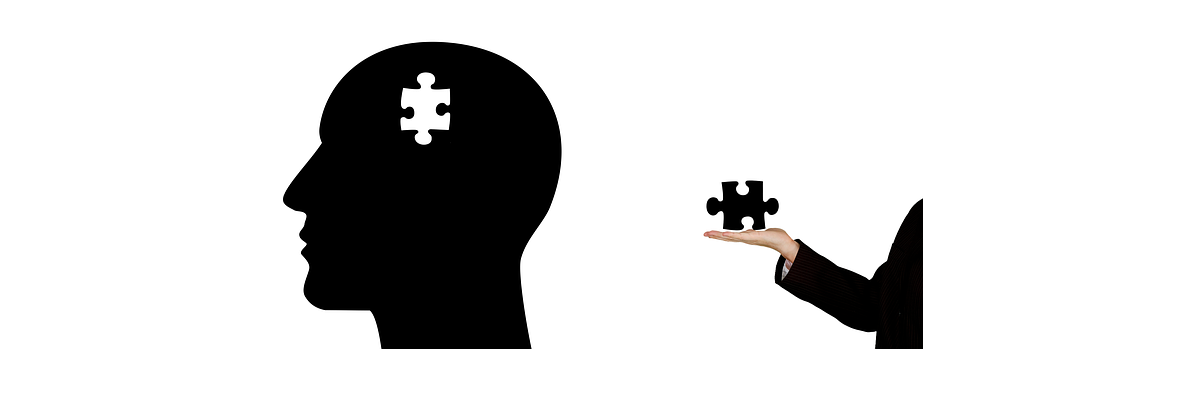 An illustration/silhouette of a bald head. A puzzle-piece is missing from inside the head. To the right of the head, a stranger’s hand extends from the frame holding the missing puzzle piece. 