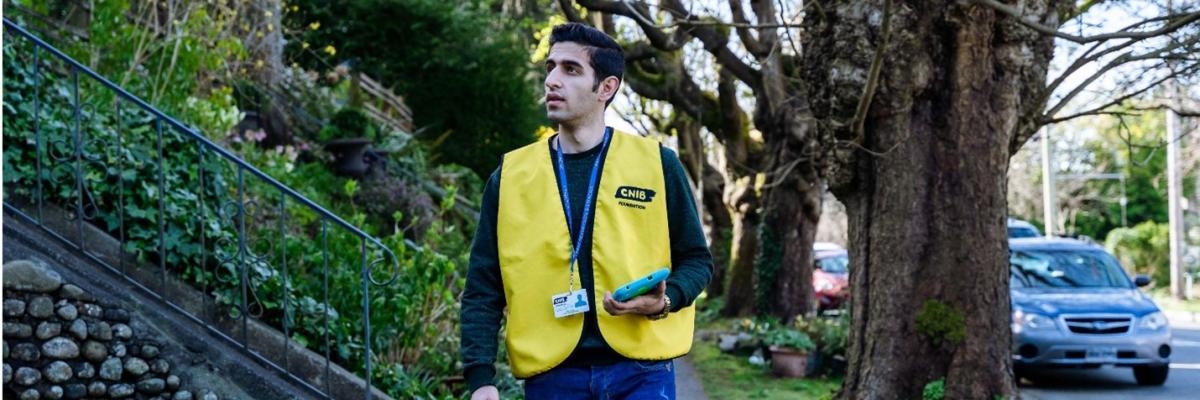 CNIB Fundraiser in a yellow vest with an ID badge and tablet