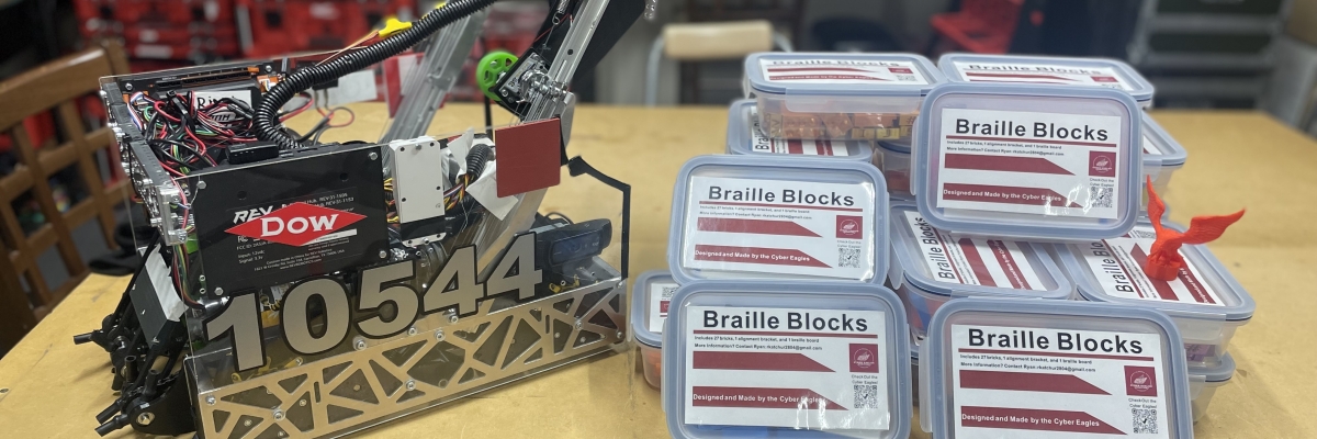A robot sits beside a stack of braille blocks on a table.