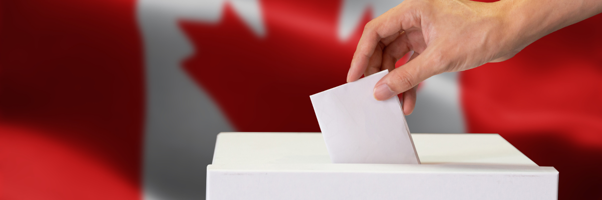 A person casting their ballot in a ballot box. A Canadian flag in the background.