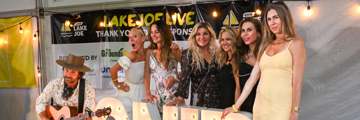 Six women wearing semi formal attire stand on a stage behind large lights in the shape of the letters C-N-I-B.