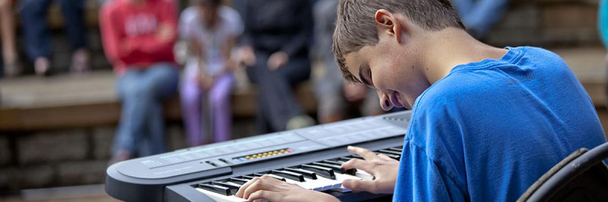 Teenage boy with sight loss playing keyboard for audience at talent show