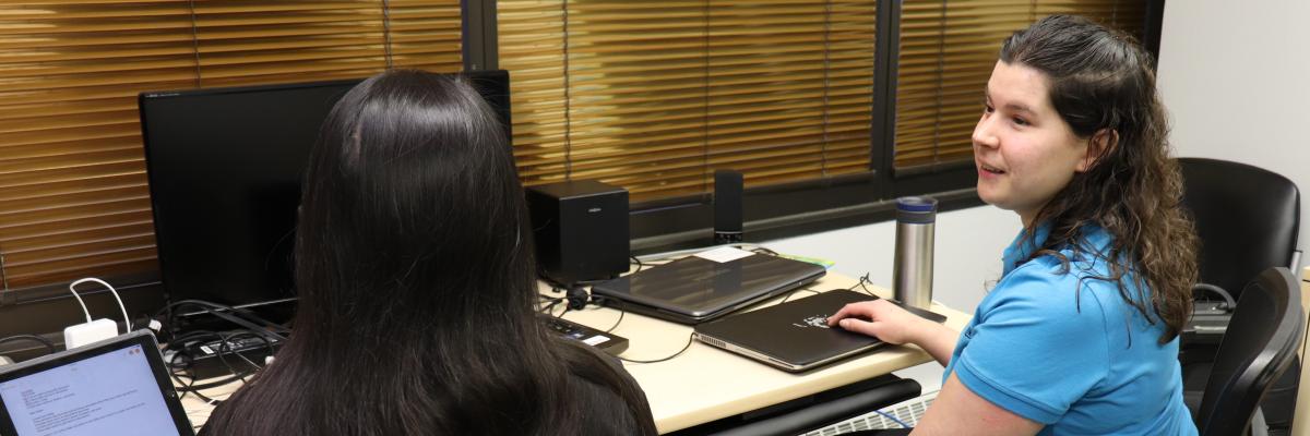 Charlene sits in front of of a computer helping a client learn technology