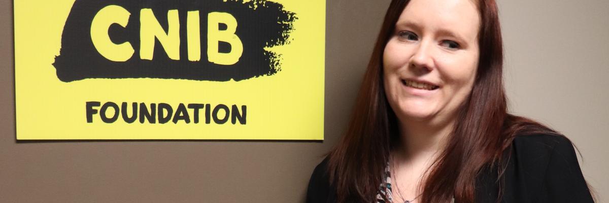 Paige Andreas smiles as she stands beside a CNIB Foundation sign