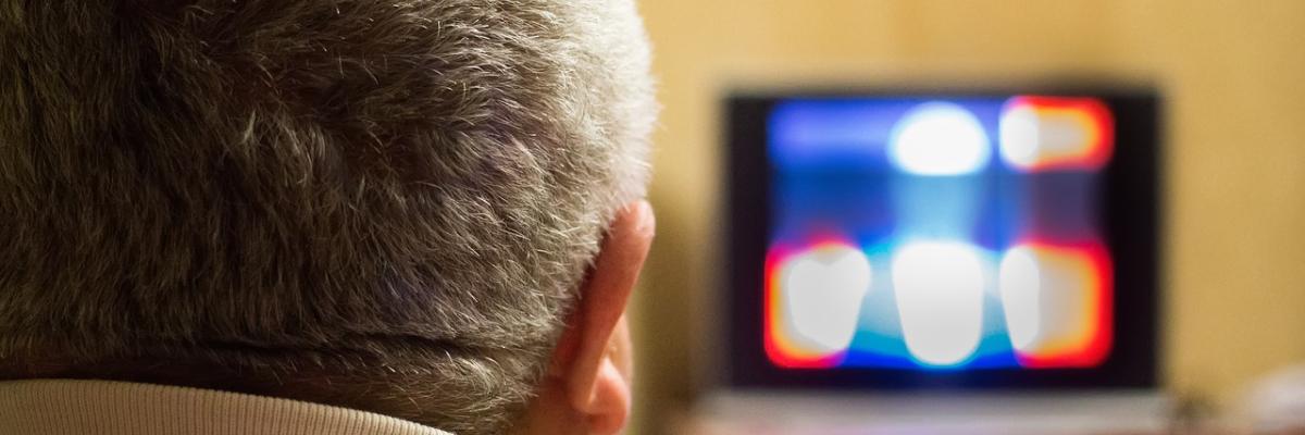 A man with grey hairs watching blury tv