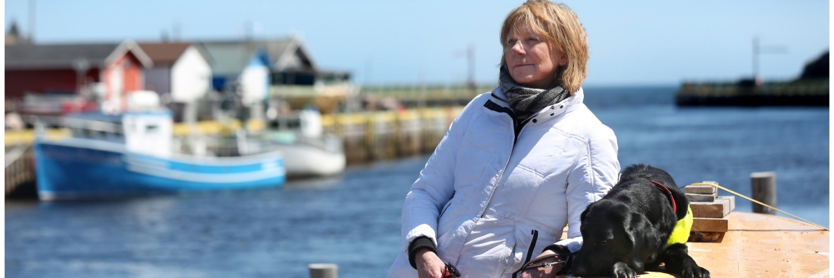 Anne Malone standing on the waterfront with her guide dog Cheryl