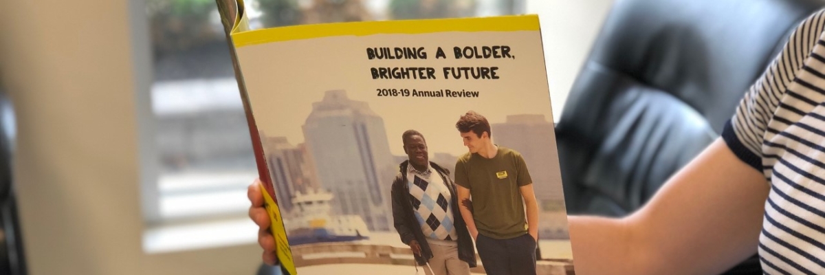 Photo of a person's hands holding an open copy of the Nova Scotia 2018-19 Annual Review