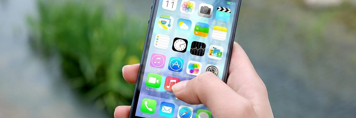 A hand holds an iPhone. Multiple apps are displayed on the iPhone screen.