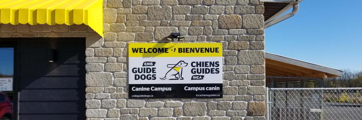A photo of the welcome sign placed on the exterior of the Canine Campus. It reads: “Welcome & Bienvenue” with the CNIB Guide Dogs logo in the middle of the sign.