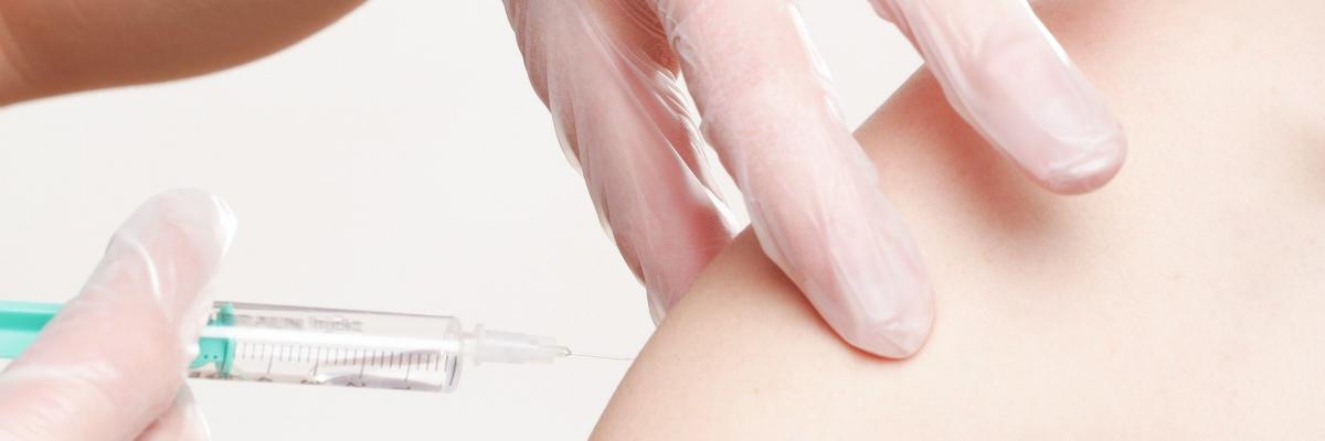 A person receiving a vaccine. A sleeveless arm is injected with a needle. 