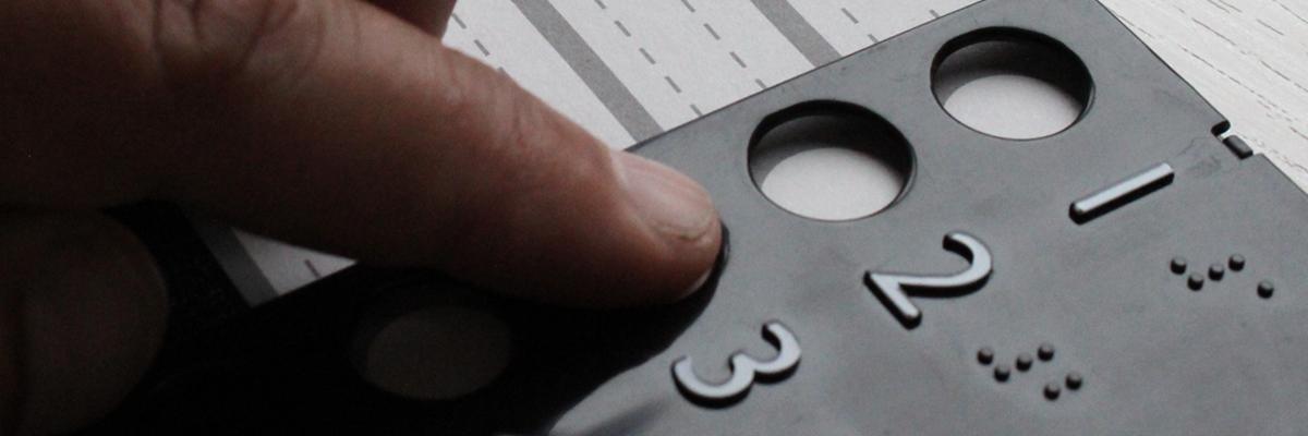 Close-up photo of a person's hands using a braille voting template.