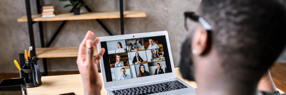 An over the shoulder shot of a young man participating in a Zoom web conference on his laptop.