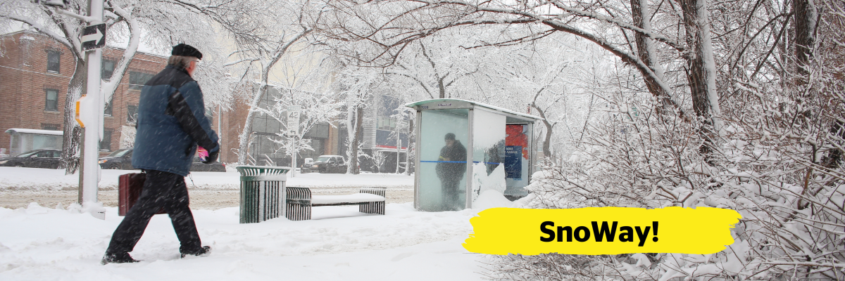 A residential street, sidewalks, and surrounding buildings are covered in snow. A man walks down a snow-covered sidewalk. To his left is a bus shelter and a bench which are also covered in snow. One person stands in the bus shelter. In the bottom right-hand corner of the image, there is a yellow banner overlay with the text “SnoWay!”