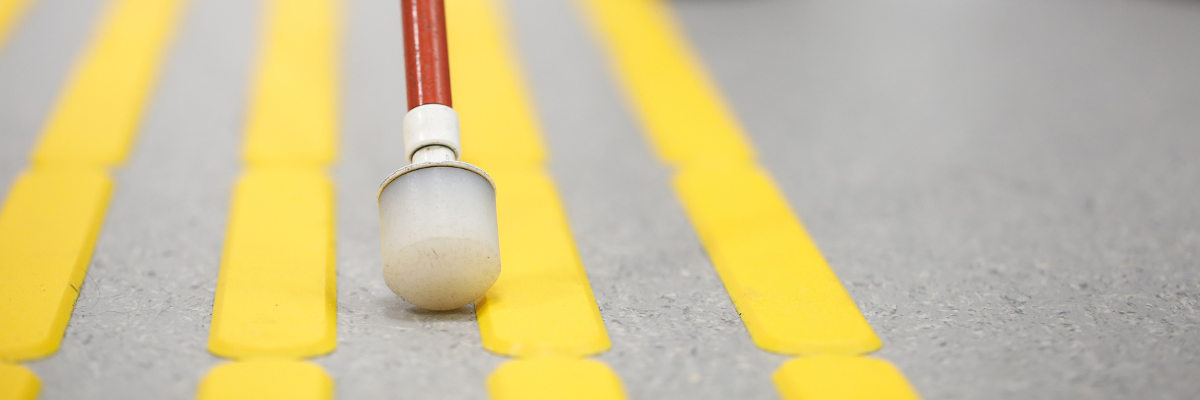 A white cane being used on pavement with raised yellow lines.